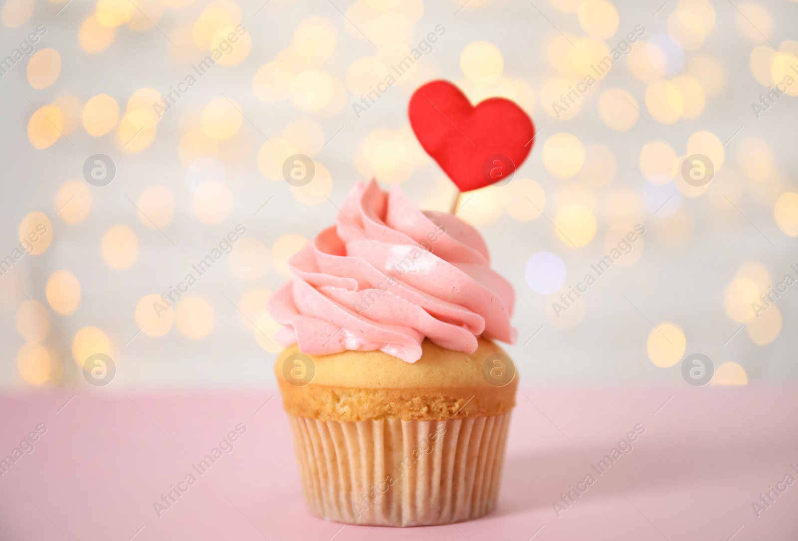 Photo of Tasty cupcake for Valentine's Day on pink table against blurred lights