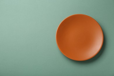 Photo of Clean orange plate on light green background, top view. Space for text