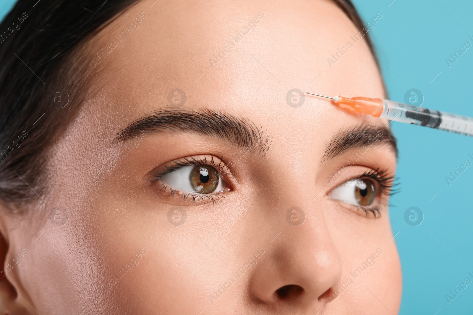 Photo of Young woman getting facial injection on light blue background, closeup. Cosmetic surgery