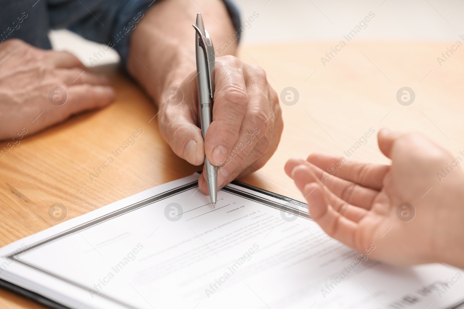 Photo of Notary showing senior man where to sign Last Will and Testament at wooden table indoors, closeup