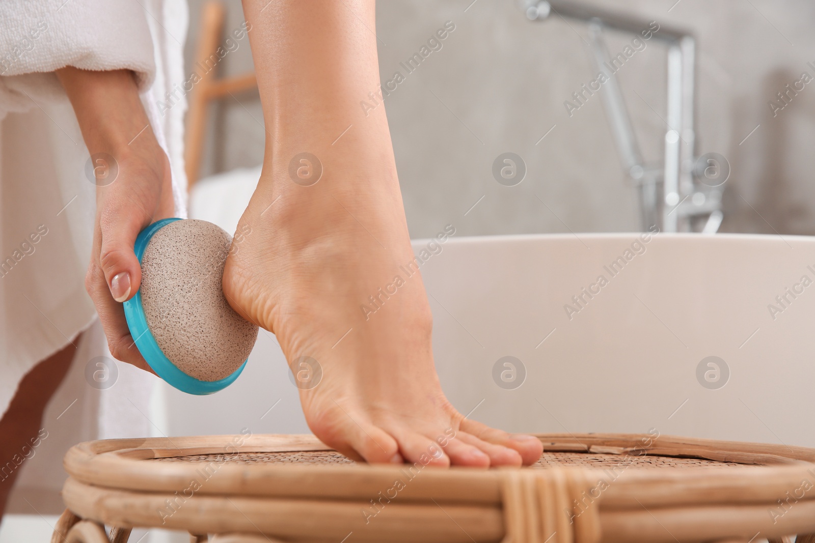 Photo of Woman using pumice stone for removing dead skin from feet in bathroom, closeup