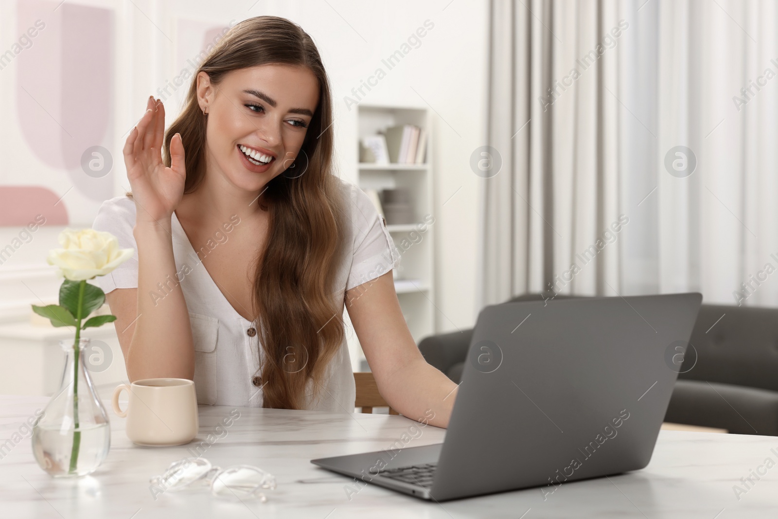 Photo of Happy woman having video chat via laptop at white table in room