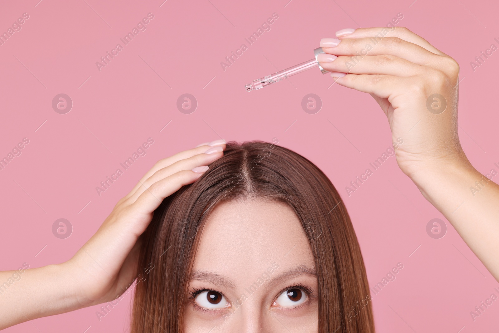 Photo of Woman applying serum onto hair on pink background, closeup