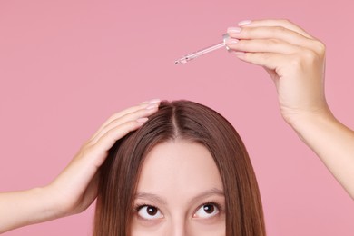 Woman applying serum onto hair on pink background, closeup