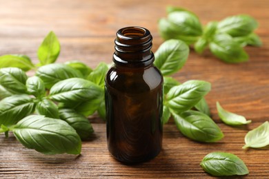 Glass bottle of basil essential oil and leaves on wooden table