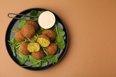 Photo of Delicious falafel balls, herbs and sauce on pale brown, top view. Space for text