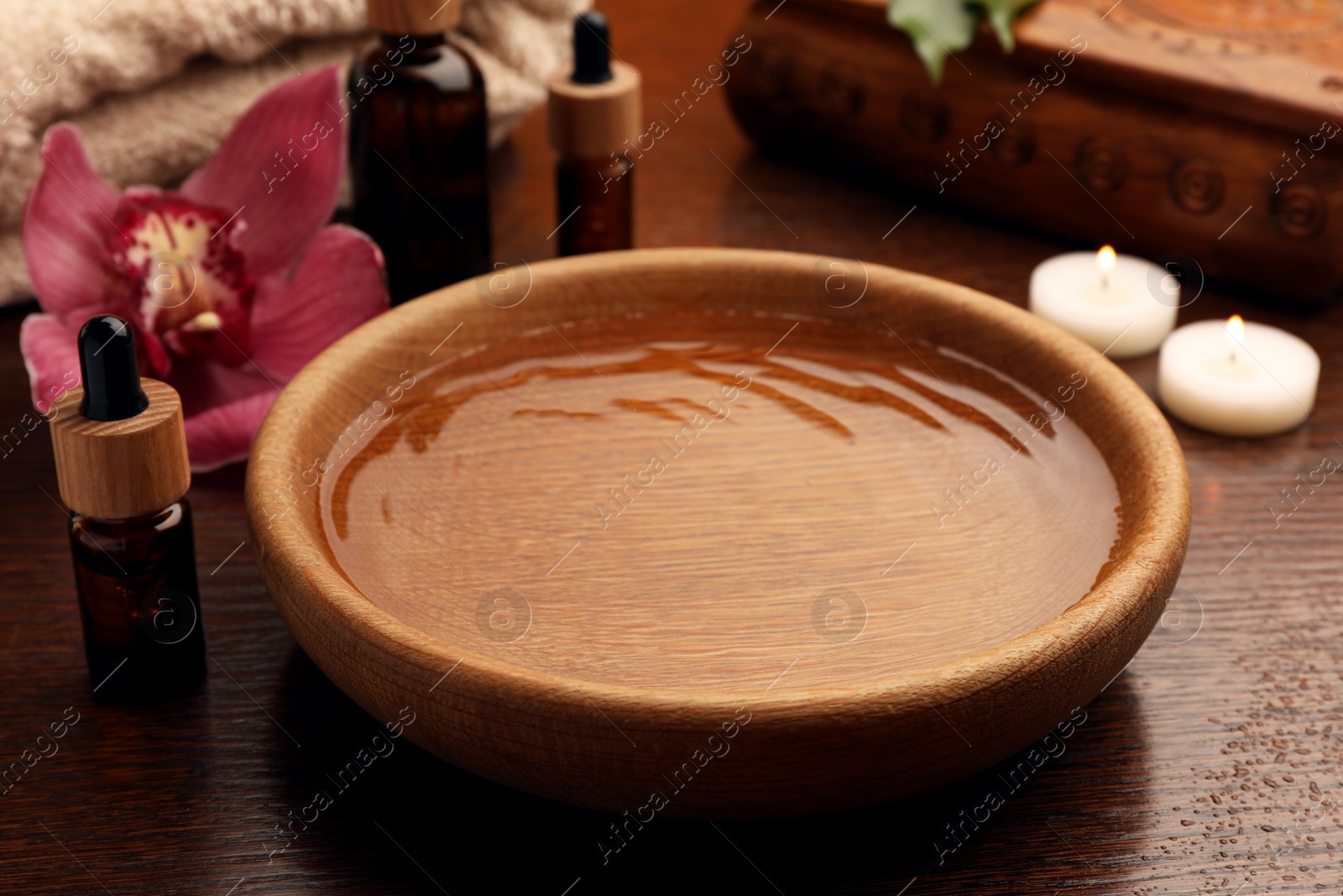 Photo of Bowl of water, bottles with essential oil and candles on wooden table. Aromatherapy treatment