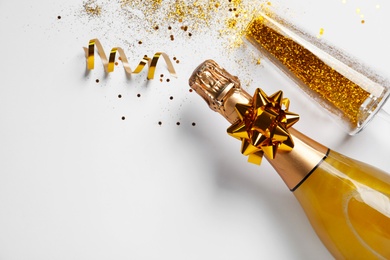 Bottle of champagne, glass with gold glitter and space for text on white background, top view. Hilarious celebration