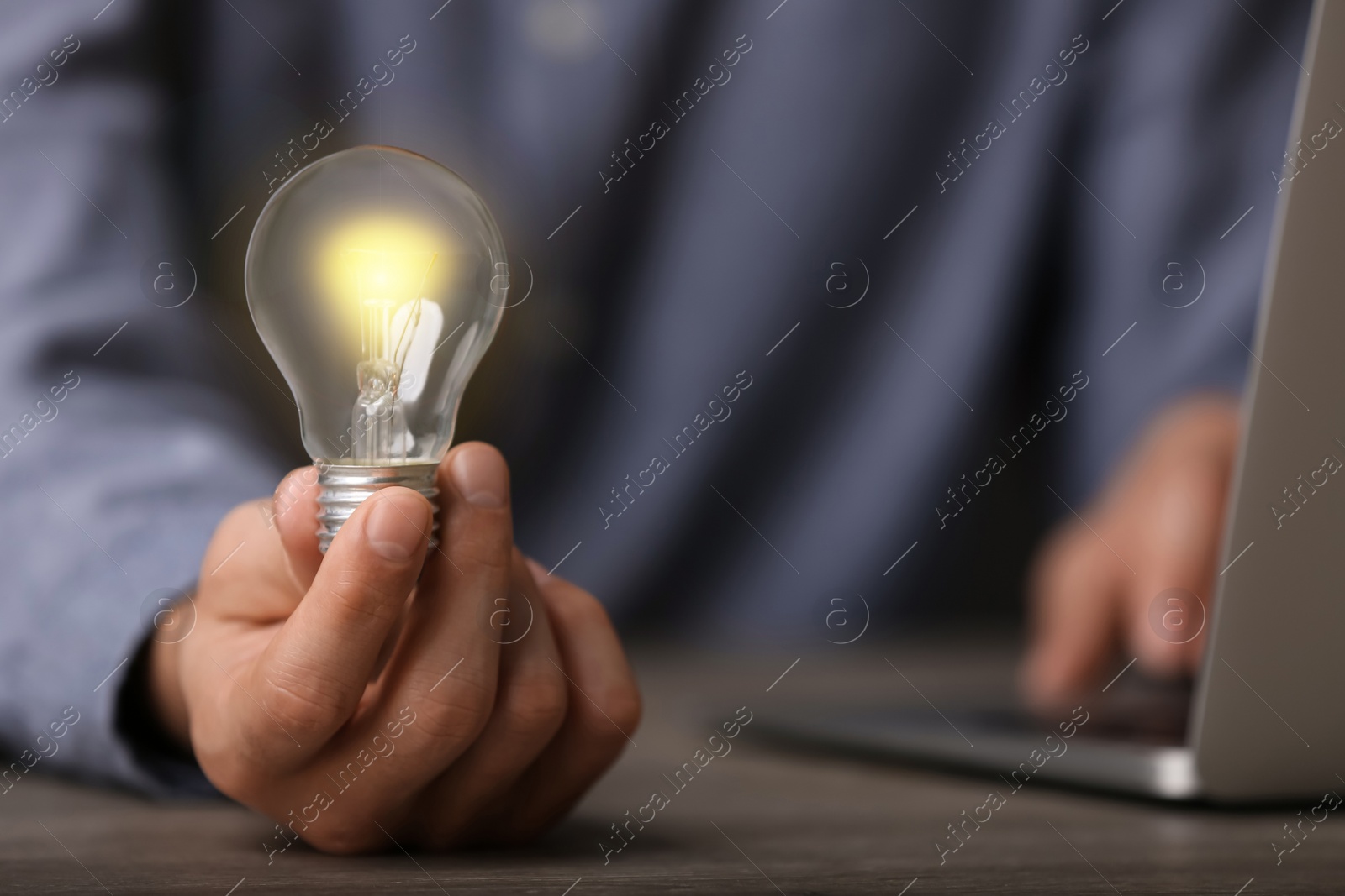 Photo of Glow up your ideas. Closeup view of man holding light bulb while working at wooden desk, space for text