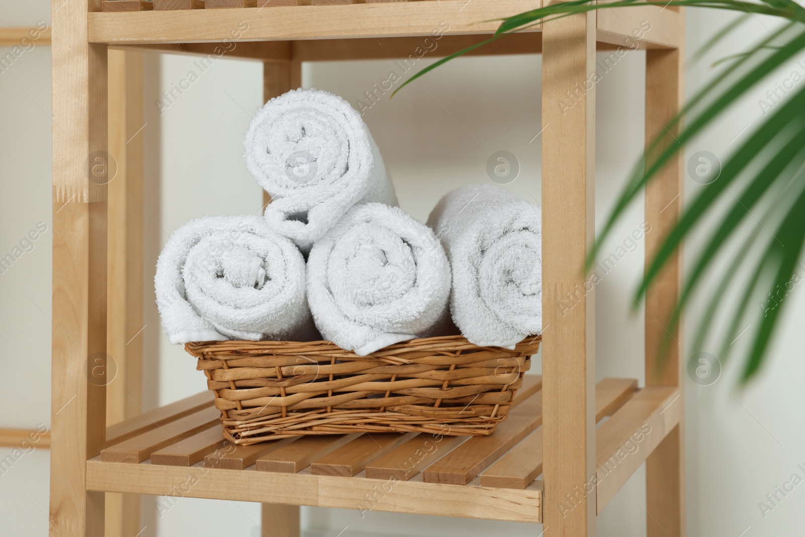 Photo of Soft folded towels in wicker basket on wooden shelving unit