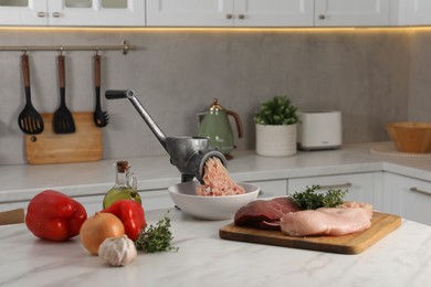 Metal meat grinder with chicken mince and products on white marble table in kitchen