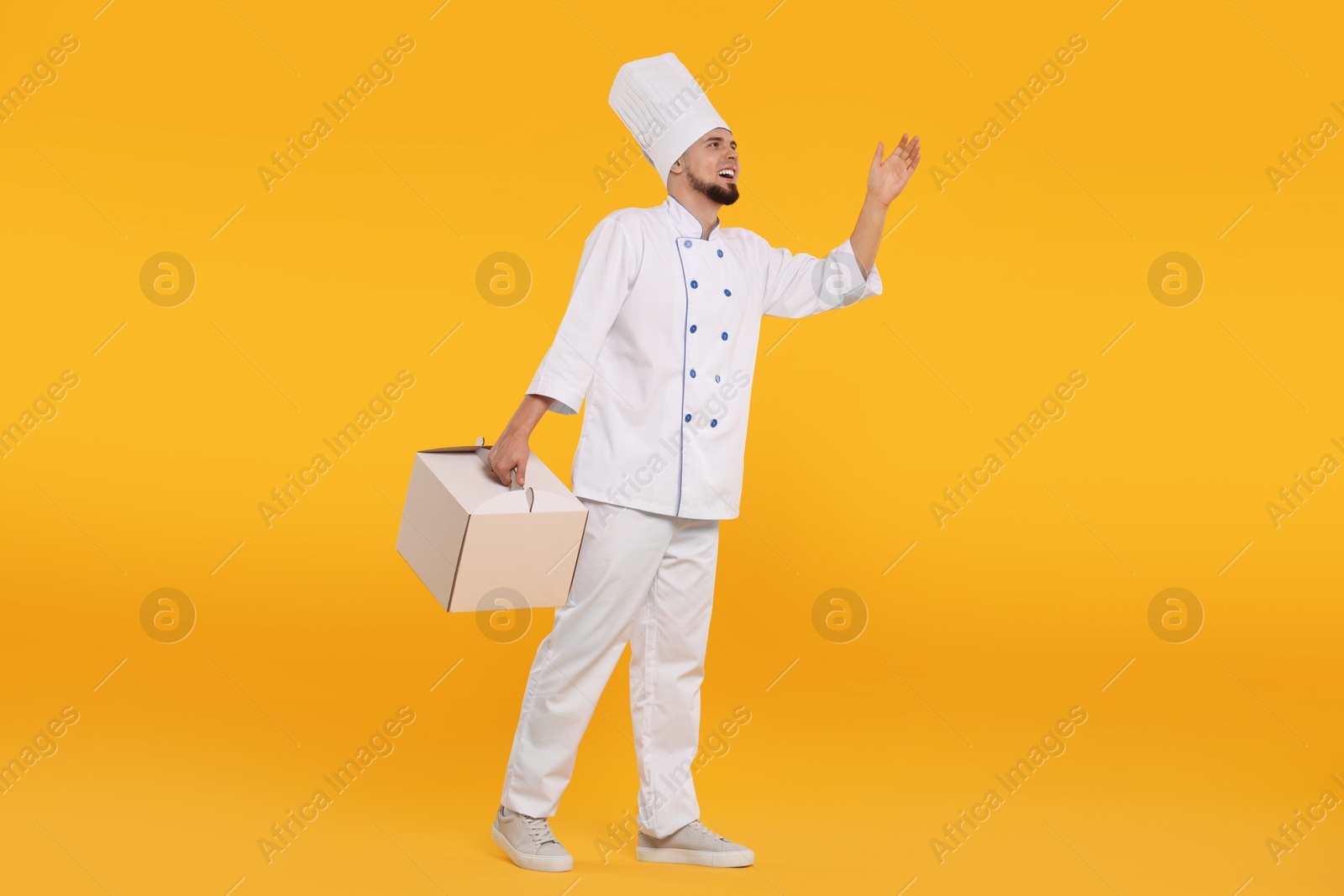 Photo of Happy professional confectioner in uniform holding cake box on yellow background