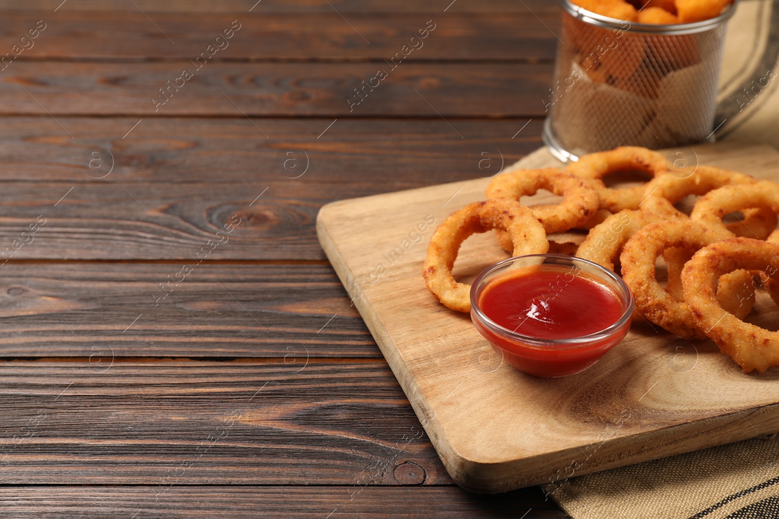 Photo of Board with tasty ketchup and onion rings on wooden table. Space for text