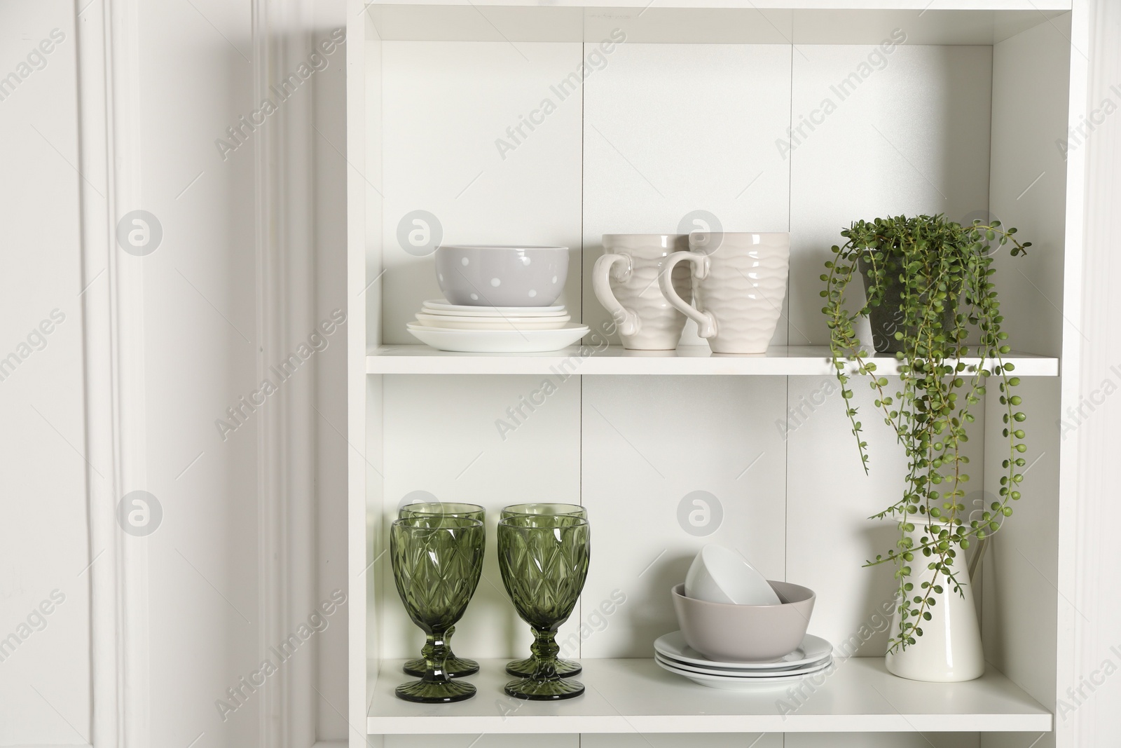 Photo of Different clean dishware and houseplant on shelves in cabinet indoors