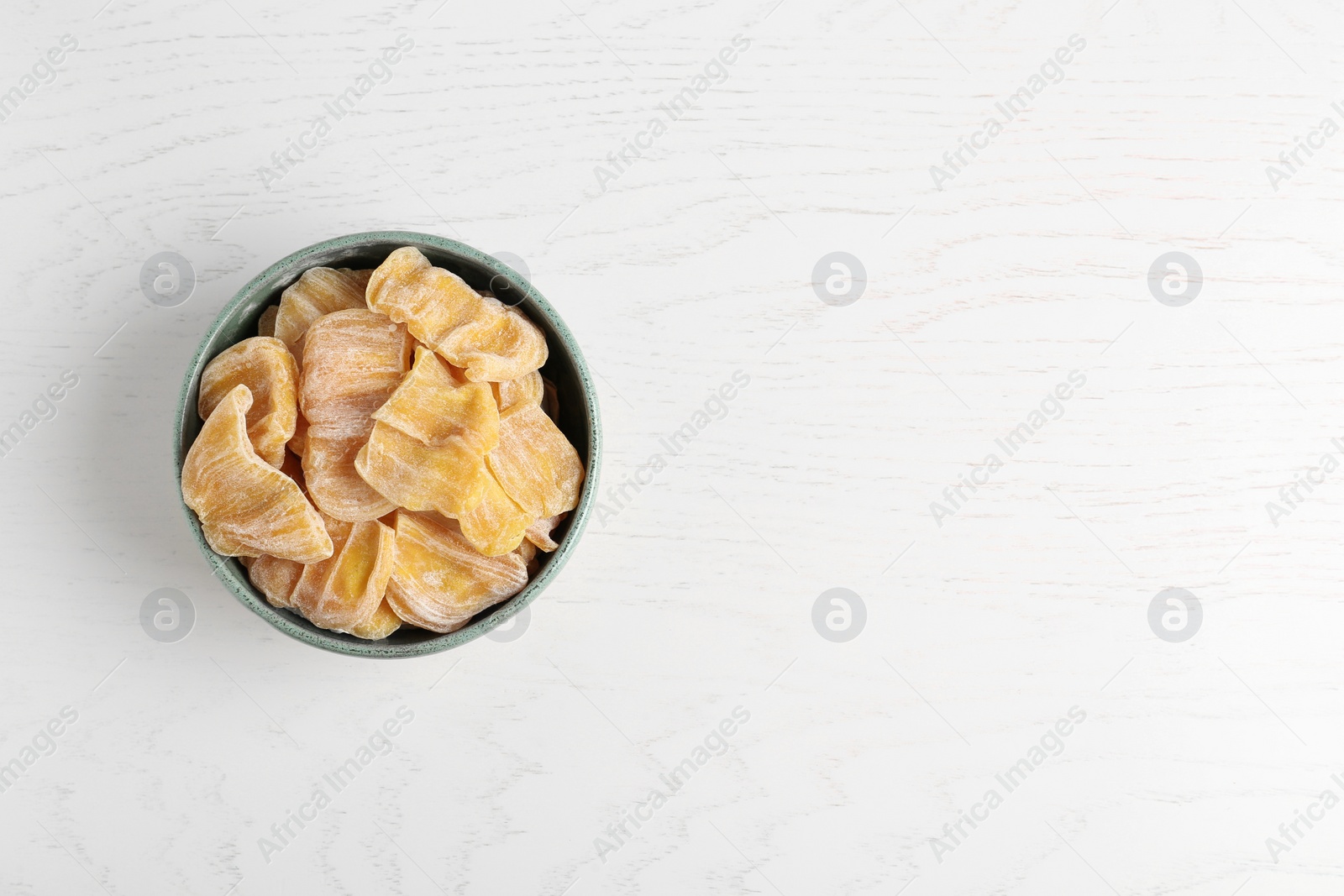 Photo of Delicious dried jackfruit slices in bowl on white wooden table, top view. Space for text