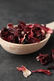 Photo of Hibiscus tea. Wooden spoon with dried roselle calyces on grey table, closeup