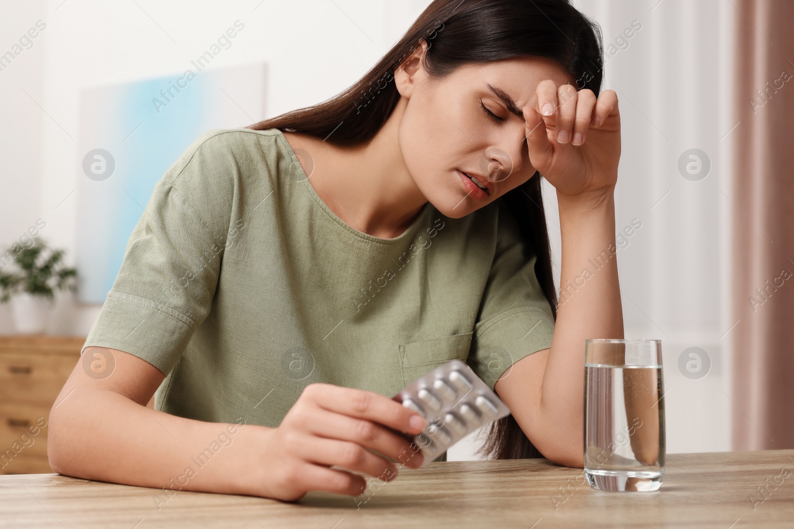 Photo of Sad woman with blister of pills suffering from headache at wooden table indoors