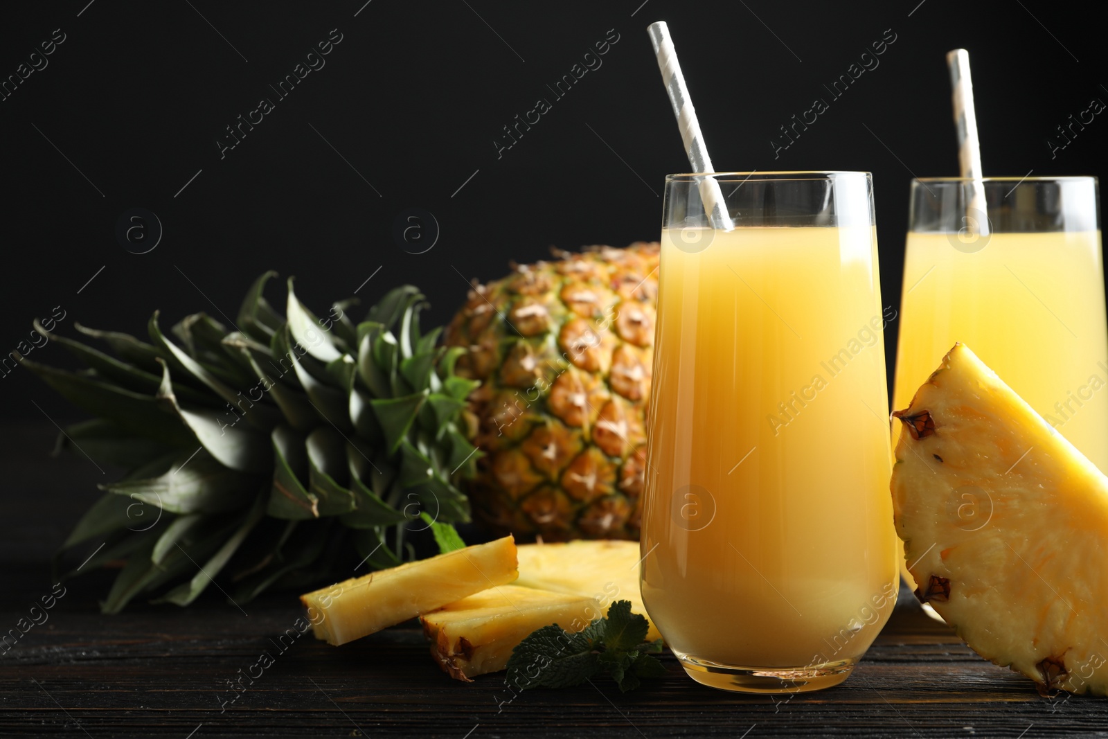 Photo of Delicious pineapple juice and fresh fruit on black wooden table, closeup