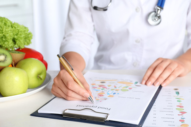 Photo of Female nutritionist with food pyramid chart at table, closeup