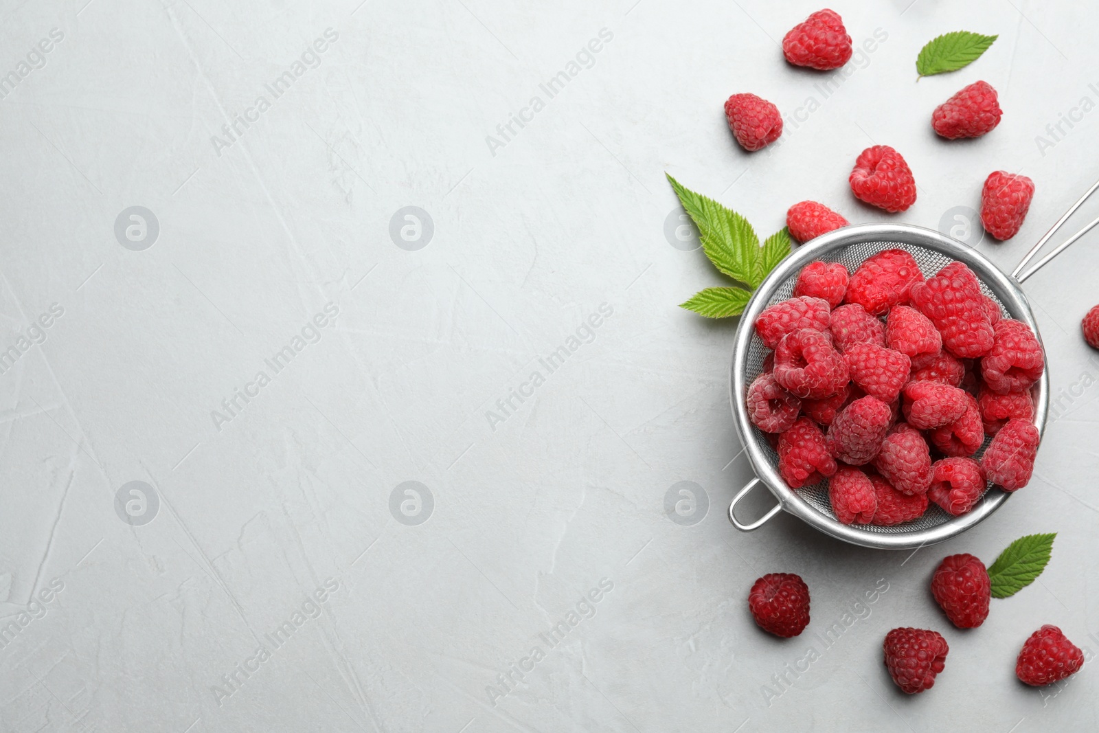 Photo of Strainer with delicious ripe raspberries on light background, top view. Space for text