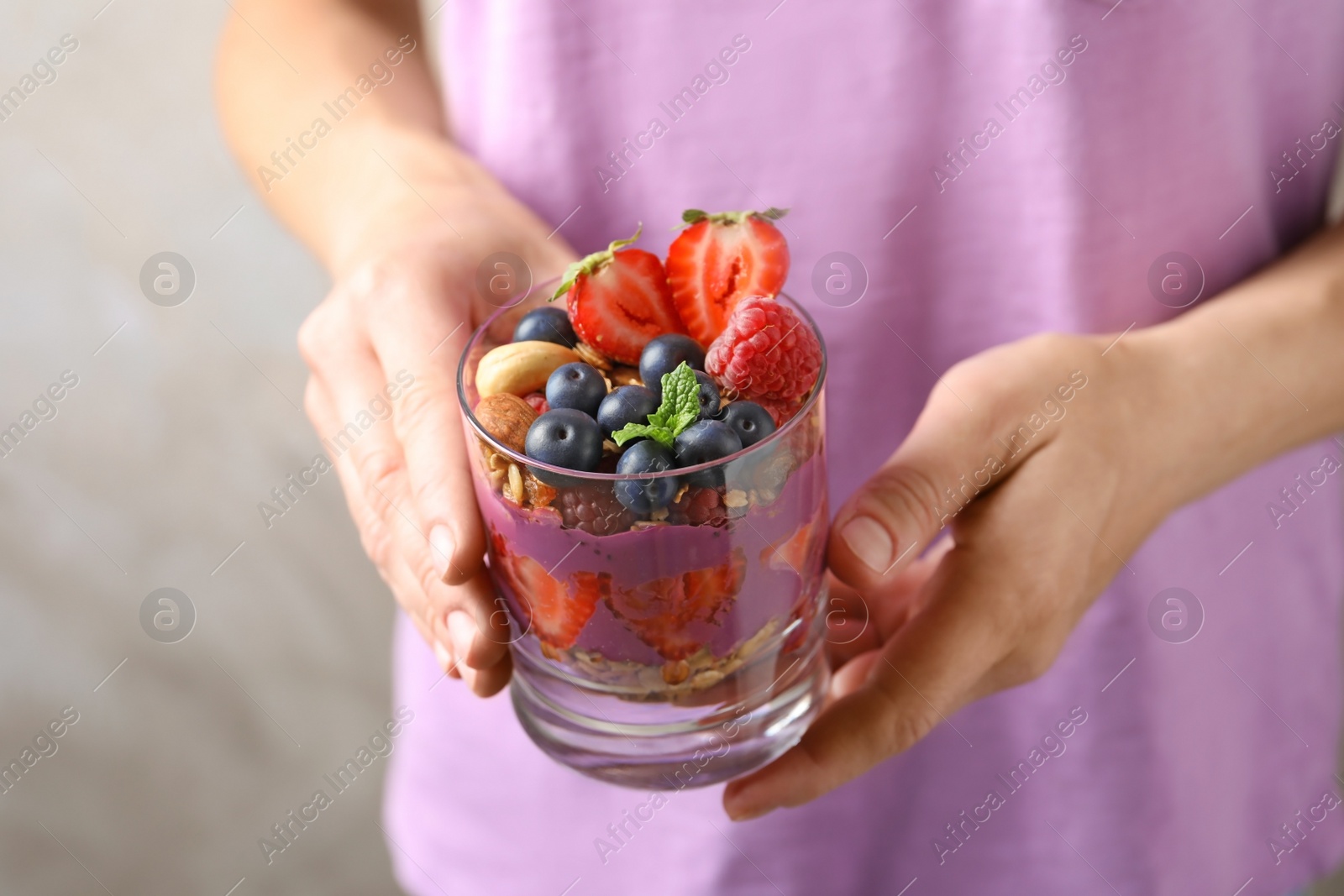 Photo of Woman holding glass of acai dessert with granola and berries, closeup