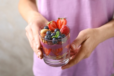 Woman holding glass of acai dessert with granola and berries, closeup