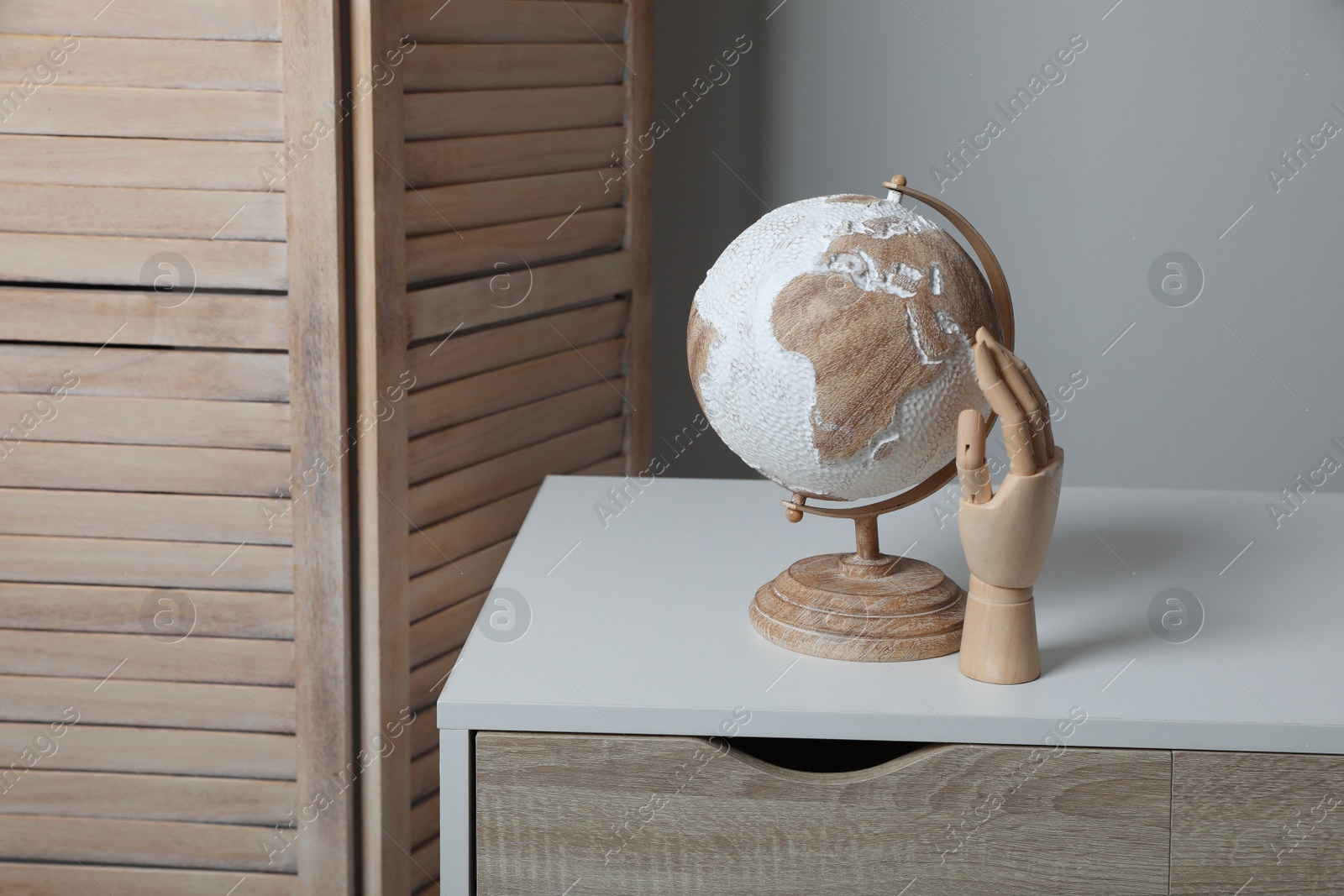 Photo of Stylish globe and wooden mannequin hand on cabinet in room