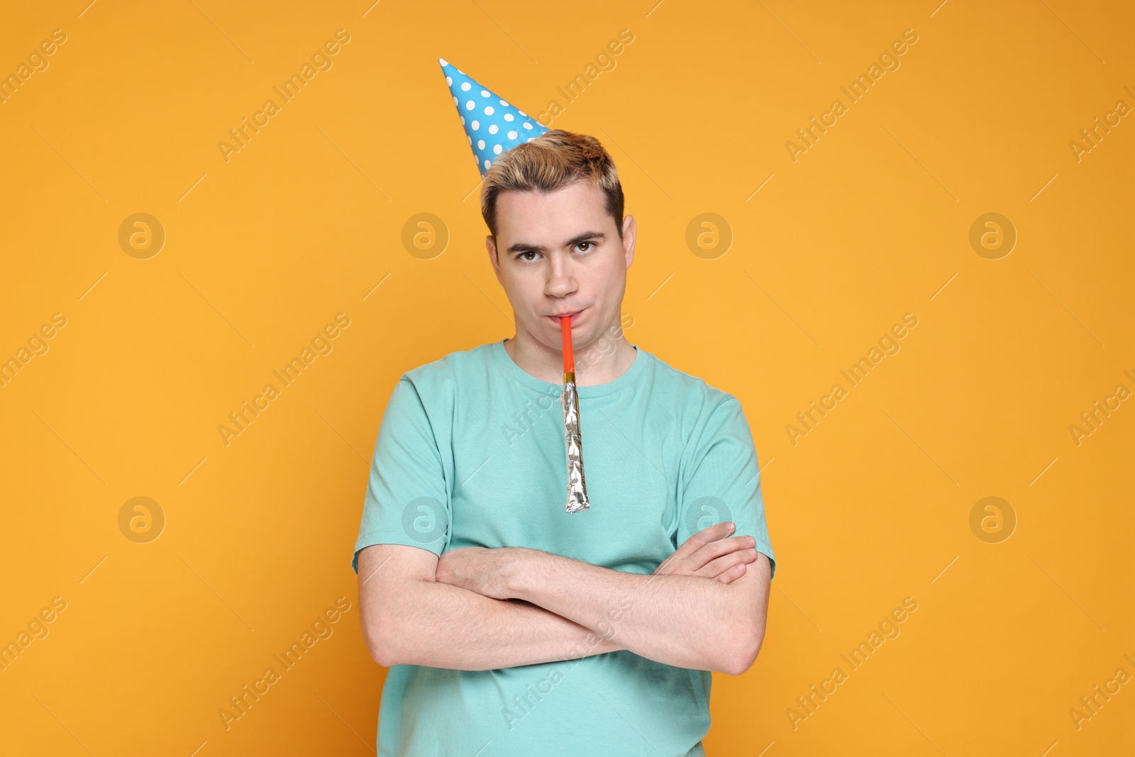 Photo of Sad young man with party hat and blower on orange background