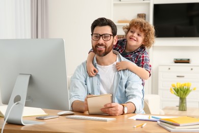Photo of Man working remotely at home. Father with his child at desk