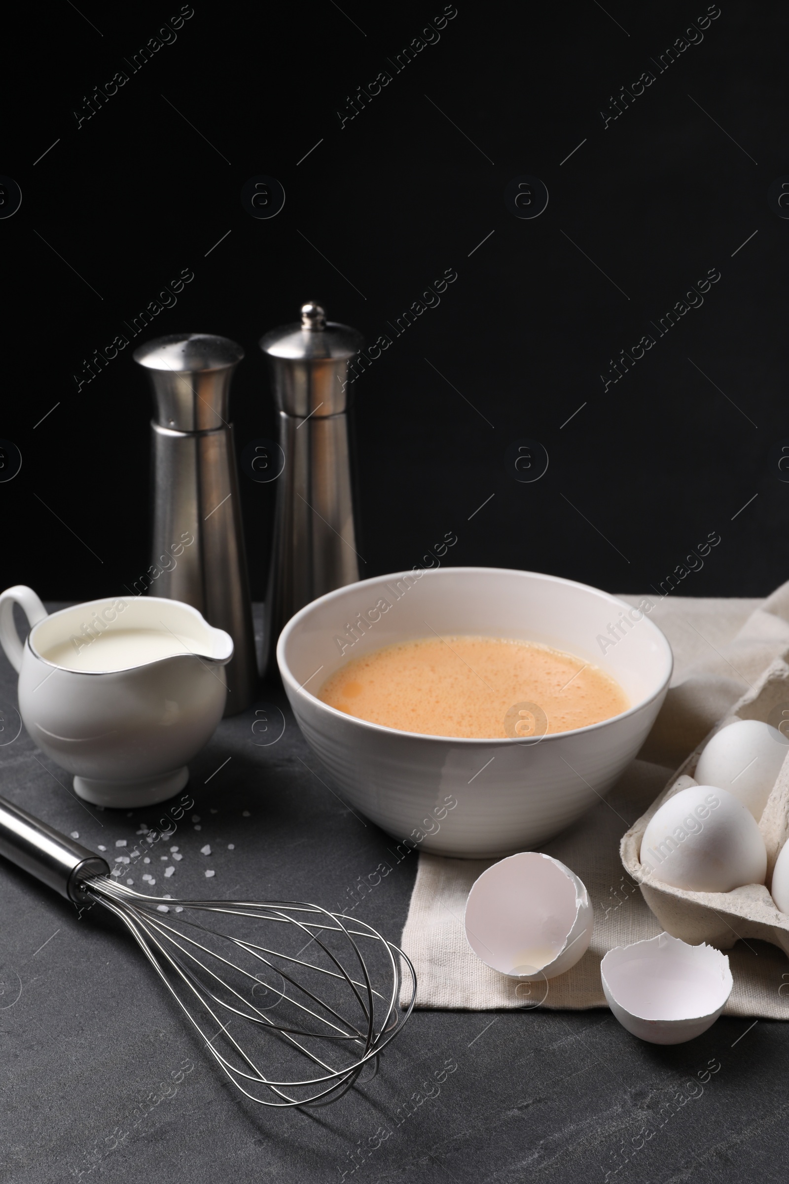 Photo of Metal whisk and dough ingredients on dark grey table