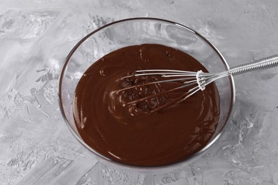 Photo of Whisk in bowl with chocolate cream on grey table, above view