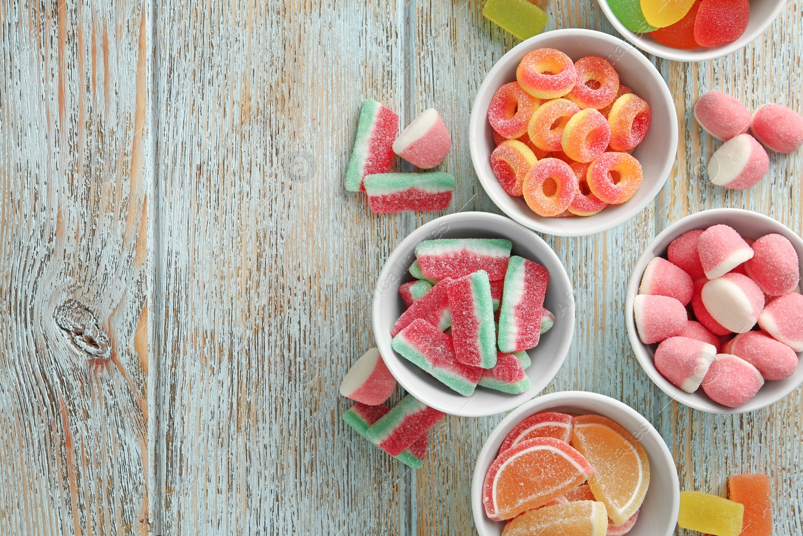 Photo of Flat lay composition with bowls of different jelly candies on wooden background. Space for text