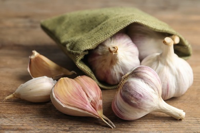 Photo of Fresh unpeeled garlic bulbs and sack on wooden table, closeup. Organic product