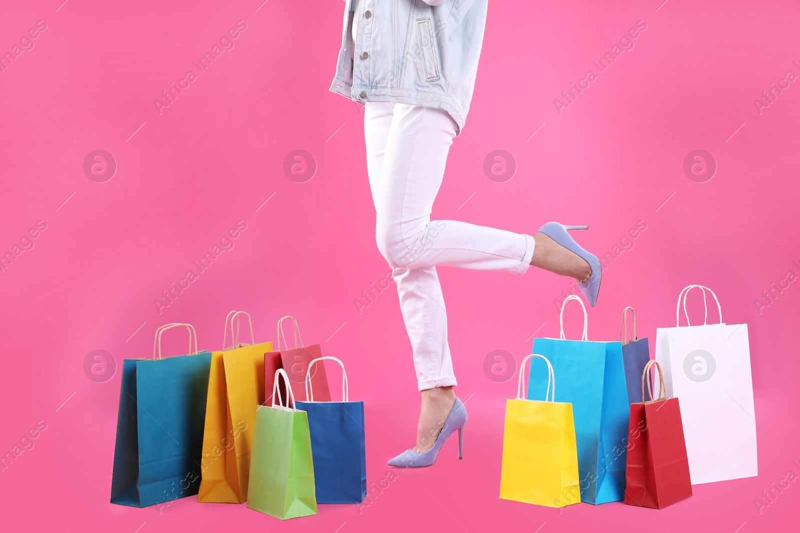 Photo of Young woman with shopping bags on color background, closeup of legs