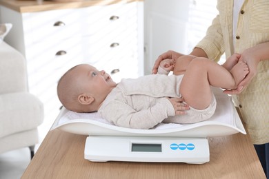 Photo of Young woman weighting her cute baby at home, closeup. Health care