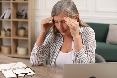 Photo of Menopause. Woman suffering from headache at wooden table indoors