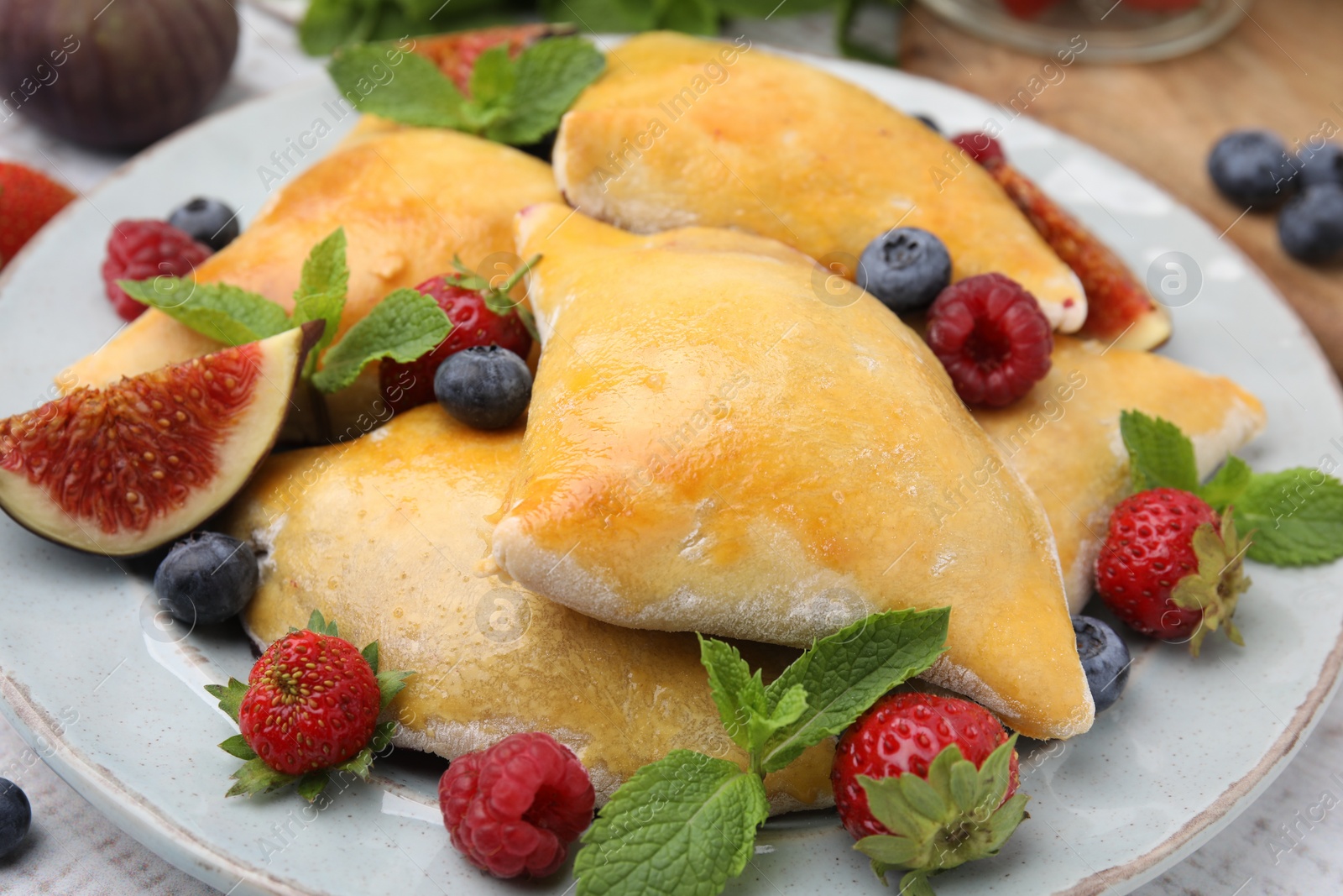 Photo of Delicious samosas with figs and berries on white table, closeup