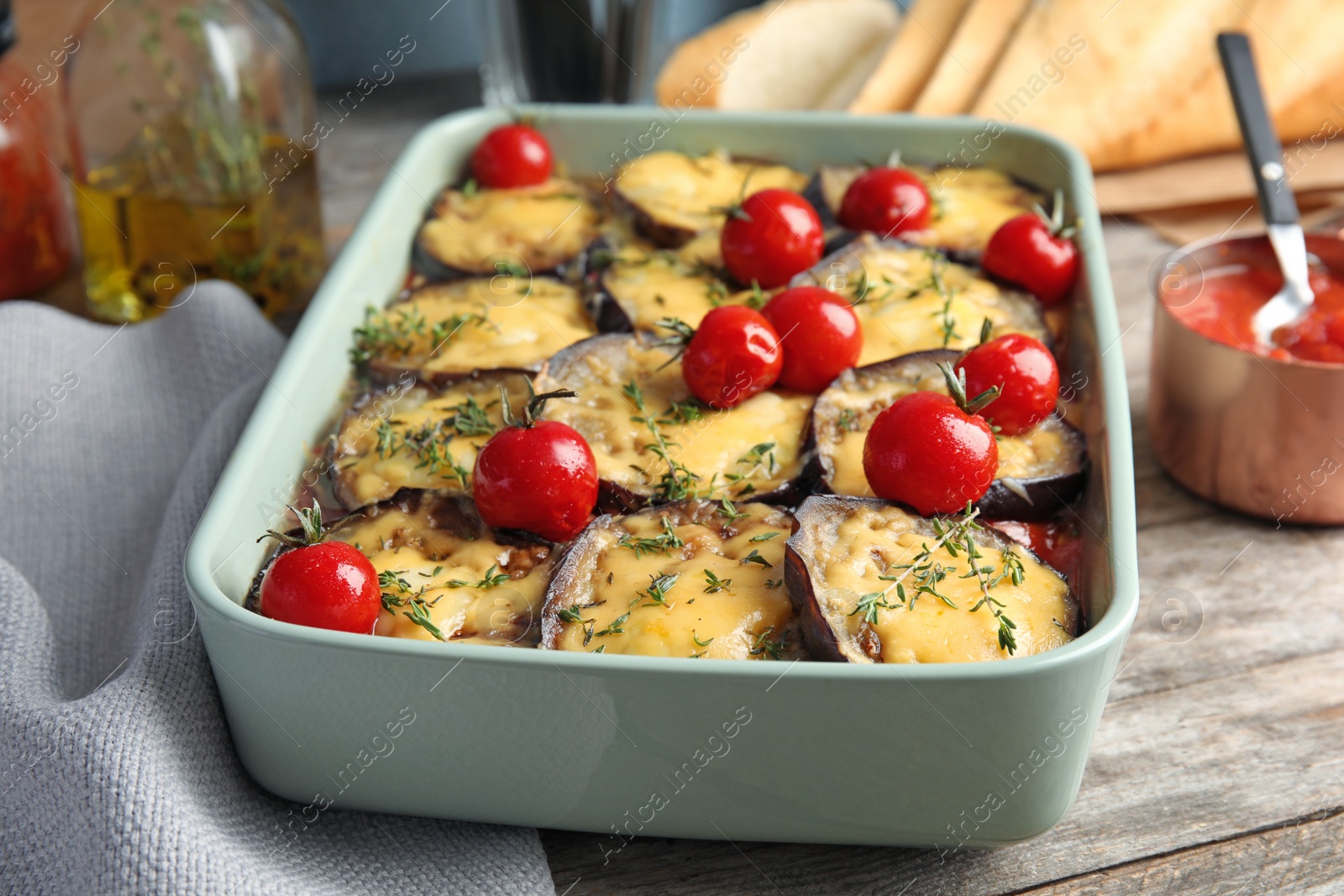 Photo of Baked eggplant with tomatoes and cheese in dishware on wooden table