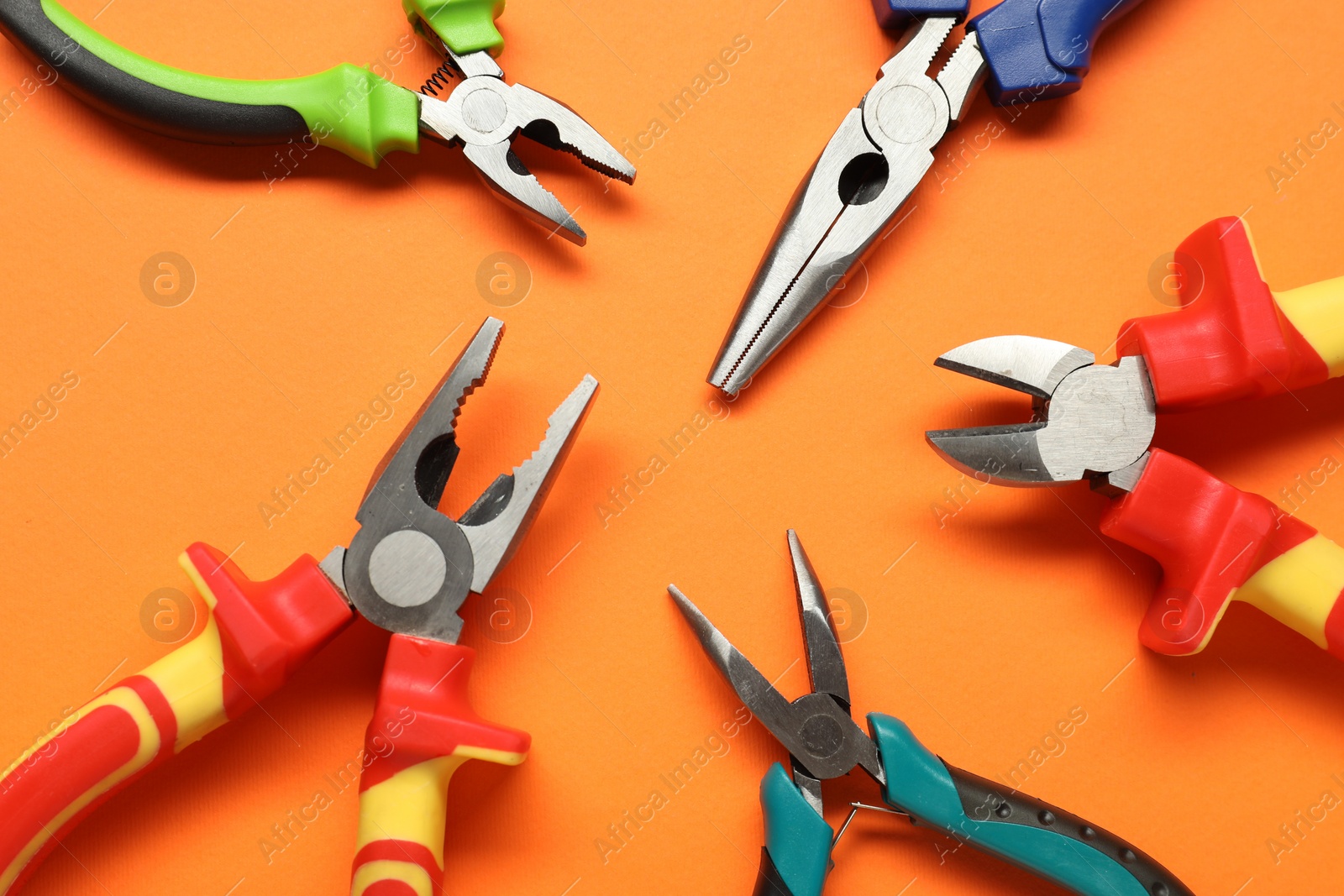 Photo of Different pliers on orange background, flat lay