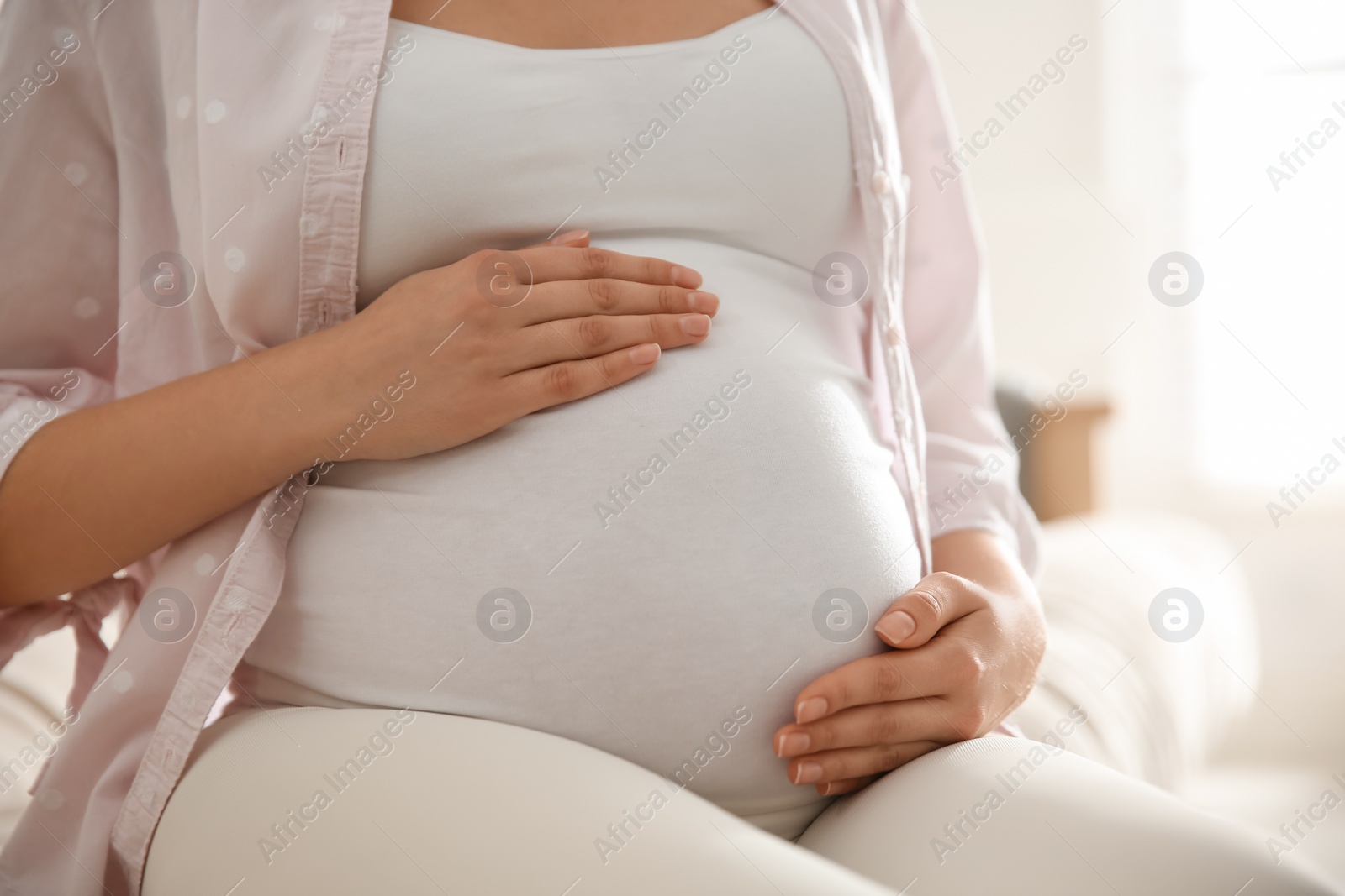 Photo of Pregnant woman touching her belly indoors, closeup