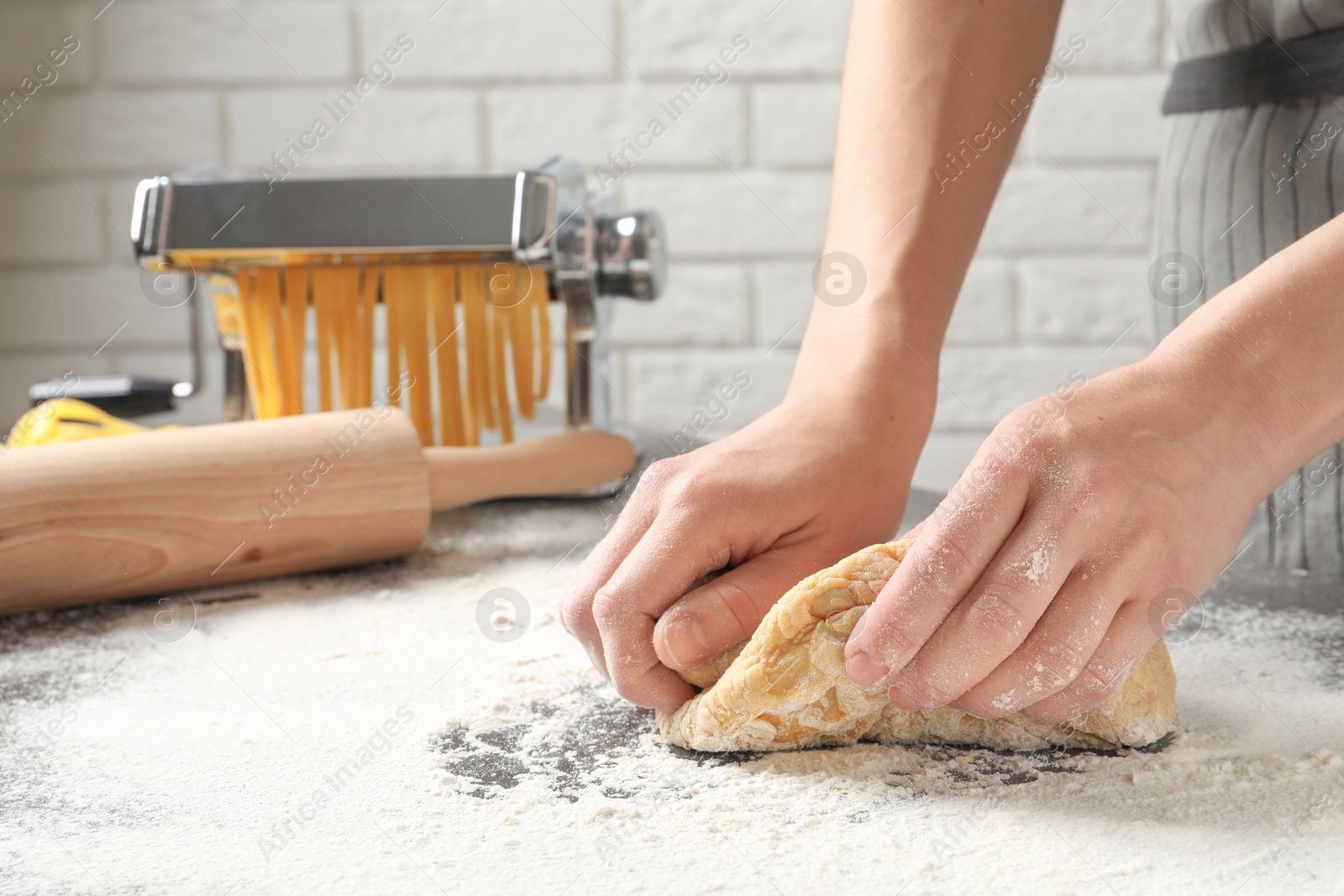 Photo of Young woman kneading dough for pasta on table