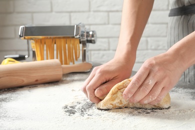 Photo of Young woman kneading dough for pasta on table