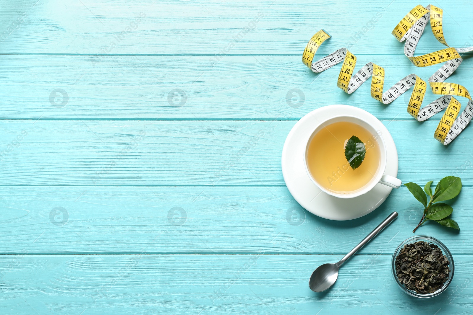 Photo of Flat lay composition with herbal diet tea and measuring tape on light blue wooden table. Space for text