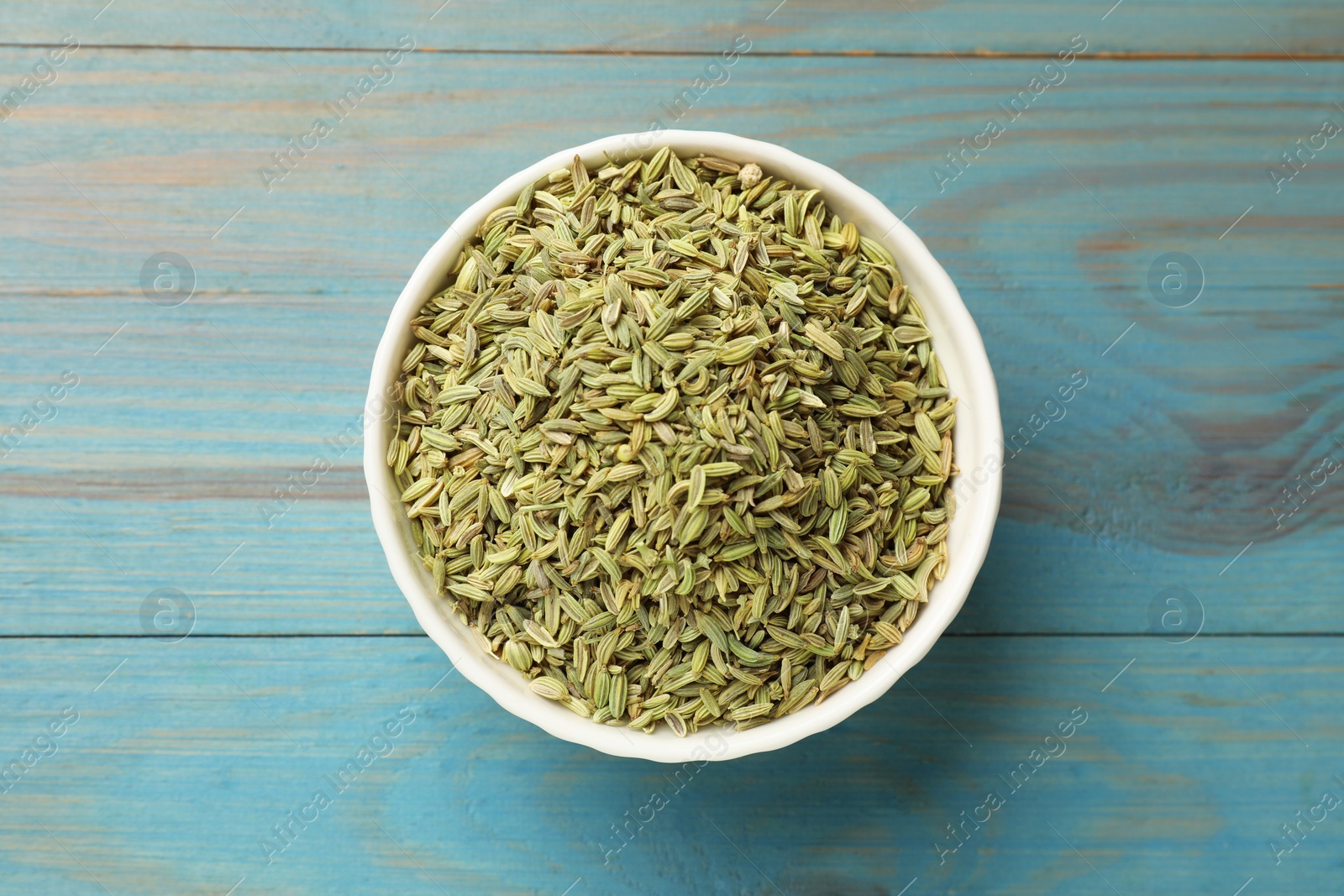 Photo of Fennel seeds in bowl on light blue wooden table, top view