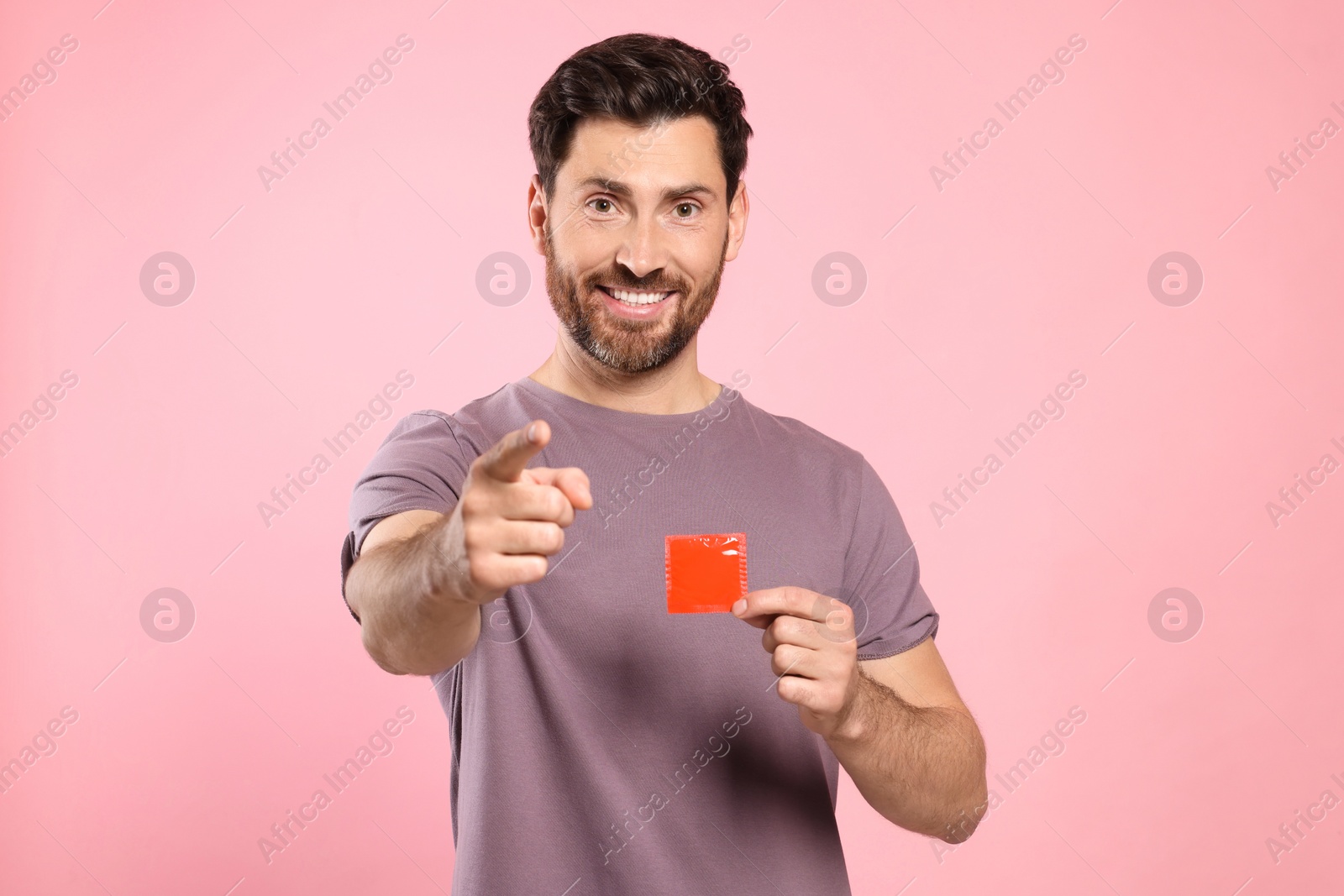 Photo of Happy man holding condom on pink background. Safe sex