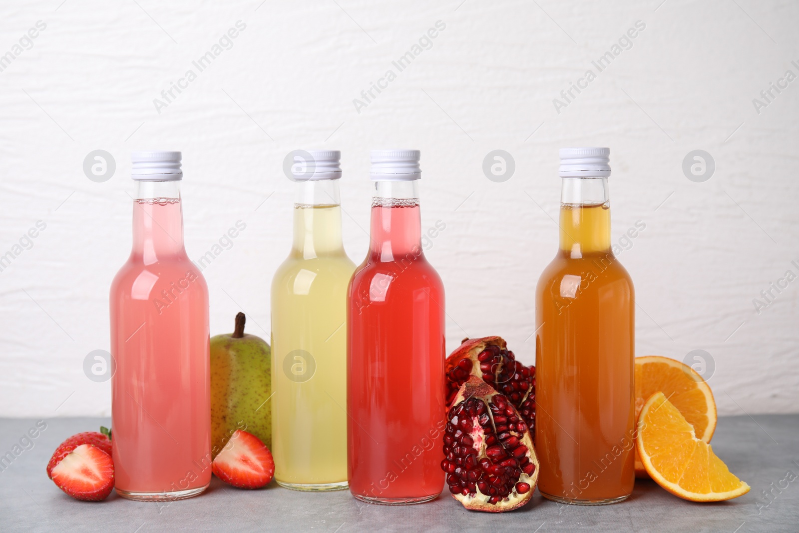 Photo of Delicious kombucha in glass bottles and fresh fruits on grey table against white background