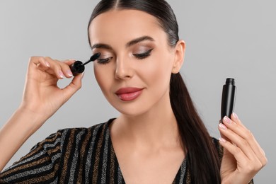 Photo of Everyday makeup. Beautiful woman applying mascara on light grey background