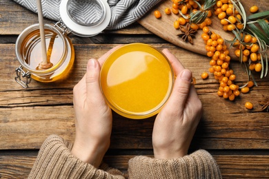 Photo of Woman with cup of fresh sea buckthorn tea at wooden table, top view