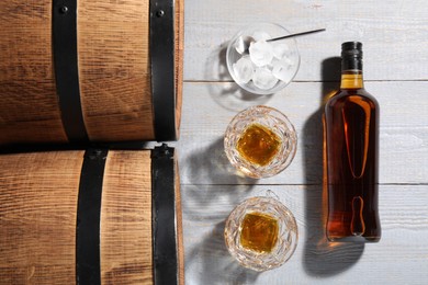 Barrels, bottle and glasses of tasty whiskey with ice cubes on light gray wooden table, flat lay