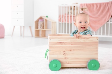 Photo of Adorable baby girl playing in wooden cart at home